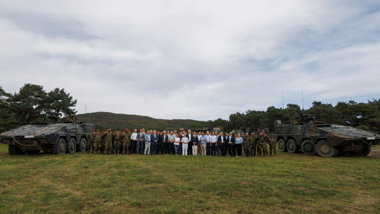 Die Abgeordneten der CDU-Landtagsfraktion NRW zu Besuch bei der größten Heereskaserne Deutschlands in Augustdorf stehen mit Soldaten und Panzern auf einer grünen Wiese.