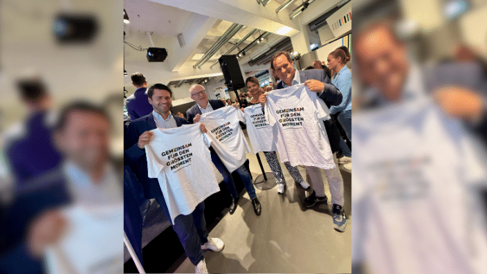 Thomas Okos, Bernhard Hoppe-Biermeyer und Thorsten Schick (v.l.) stehen mit einem T-Shirt für die Bewerbung Köln Rhein Ruhr in der Hand im Deutschen Sport & Olympia Museum in Köln